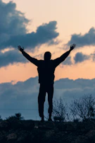 A silhouette of a person standing strong on a rocky path, arms raised in worship against a glowing horizon.