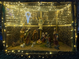 Families gathered around a warmly lit nativity scene under softly falling snow.