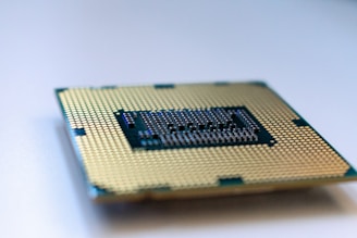 A close-up view of a computer processor chip lying on a surface, showing its intricate gold-colored pins and patterns. The focus is on the detailed grid-like design, with slight blurring at the edges.