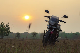 A warm photo of a motorcycle parked beside a rustic farmhouse under a wide open sky at sunset.