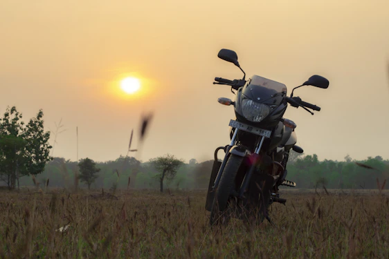 A warm photo of a motorcycle parked beside a rustic farmhouse under a wide open sky at sunset.