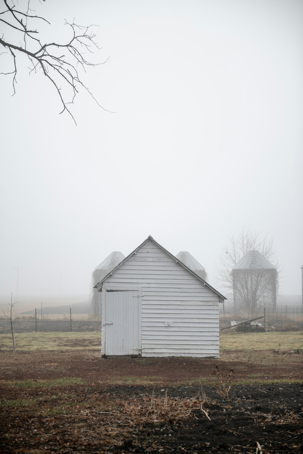 a white barn and silo in a field on a foggy day