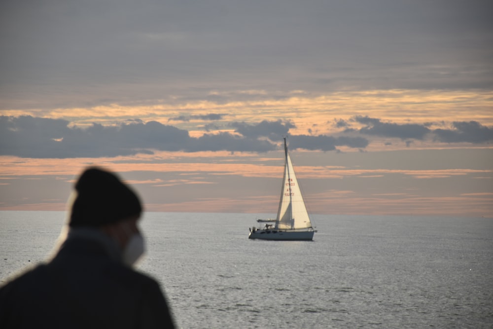 a man standing in front of a sailboat in the ocean