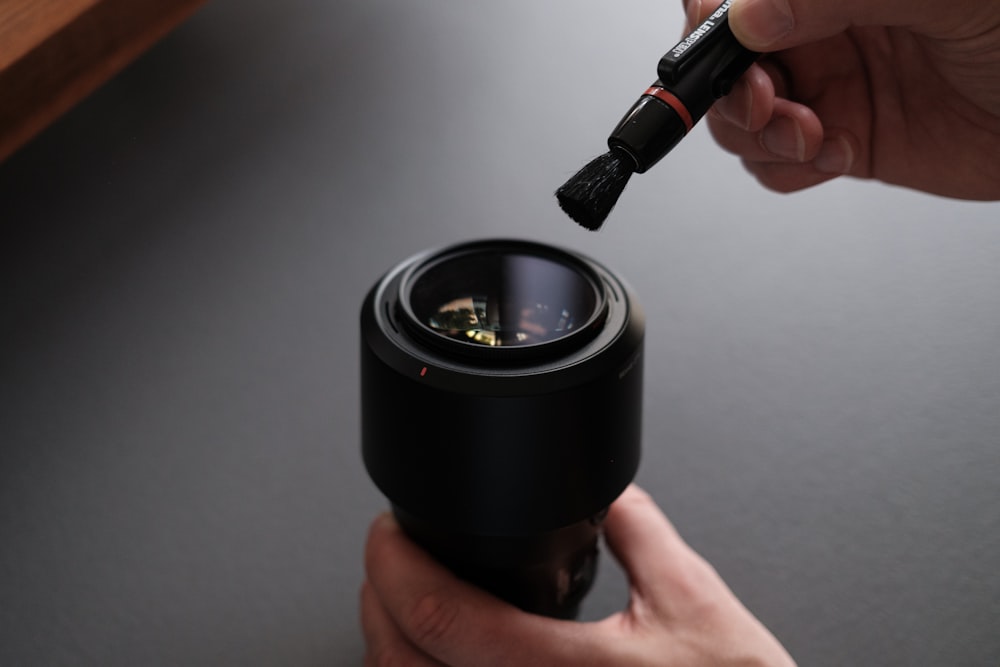 a person is holding a camera lens with a small brush