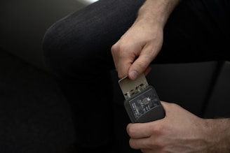 A person uses a small tool to manipulate a card or device, possibly involving a card reader or another compact gadget. The individual's hands are focused on the object, showing concentration.
