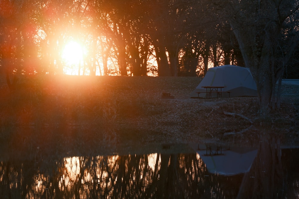 the sun is setting behind a tent in the woods