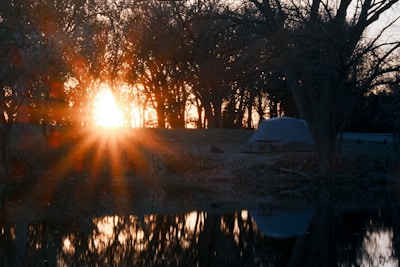A serene lakeside campsite at dawn with a sleek red tent and a vintage camera resting on a wooden picnic table.