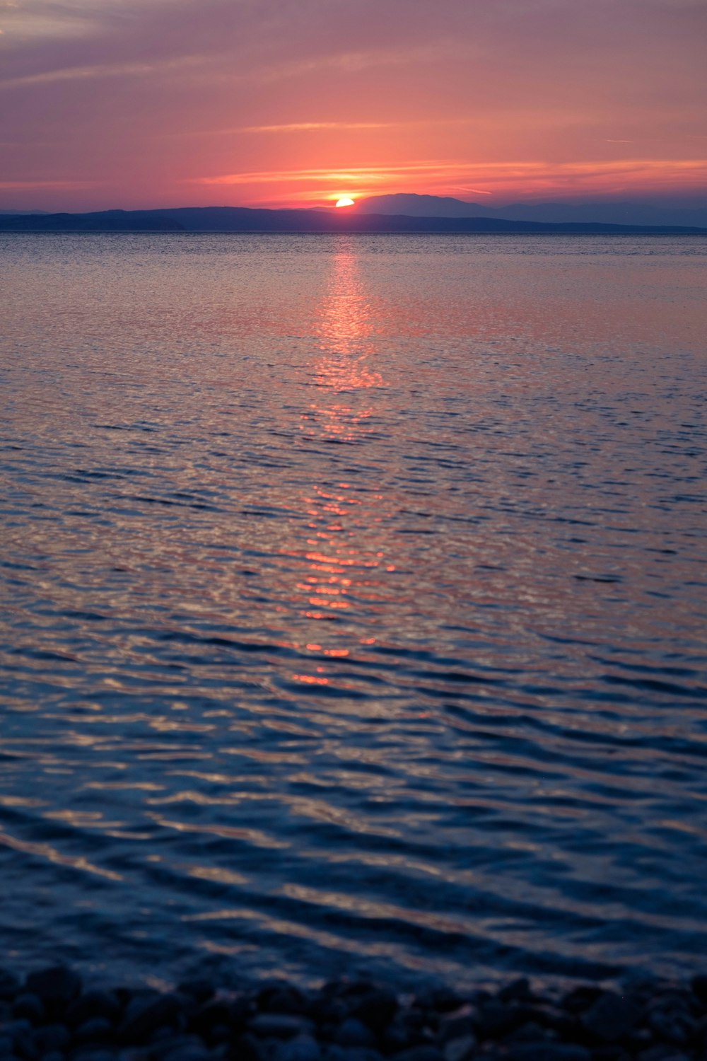 the sun is setting over the ocean with a boat in the water