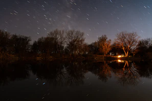 Campfire glowing warmly under a star-filled sky beside a tranquil lake