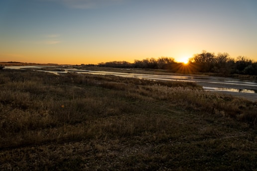 A serene landscape of Vrindavan, featuring lush greenery and a peaceful river under a soft golden sunset.