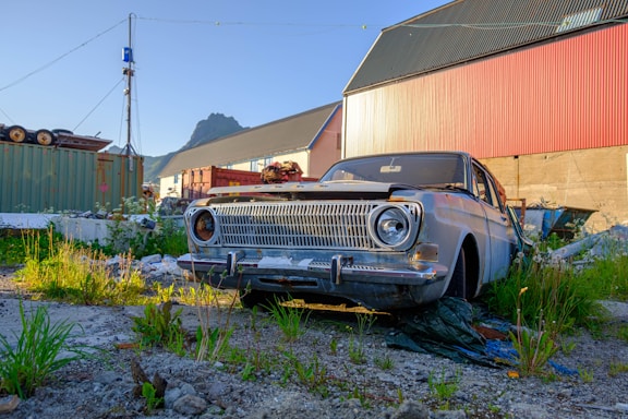 An old car is parked in a yard with overgrown grass.