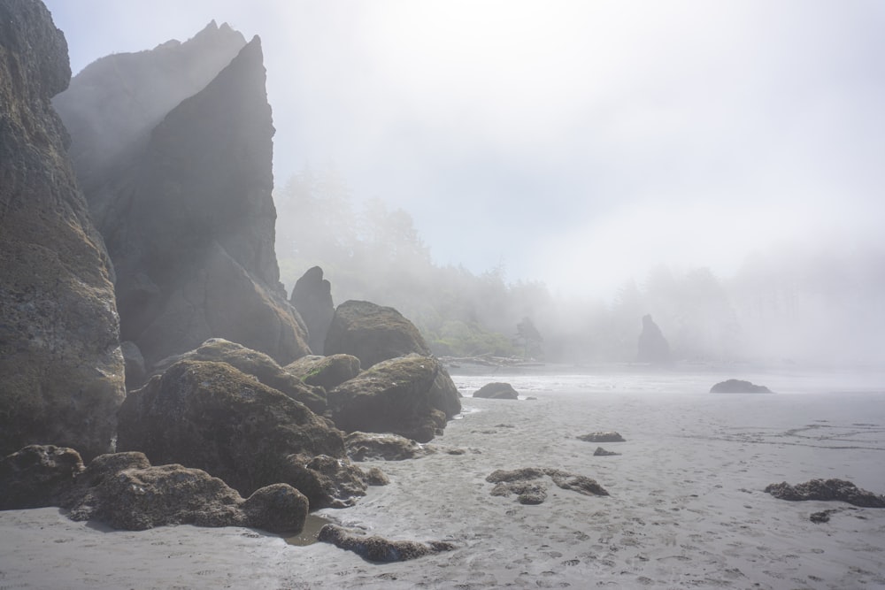 a foggy day at the beach with rocks and water