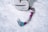 A pink and teal ice axe lies on a snowy surface next to a white backpack. The axe has a curved handle with a sturdy grip, designed for climbing. The backpack appears worn and is lightly dusted with snow.