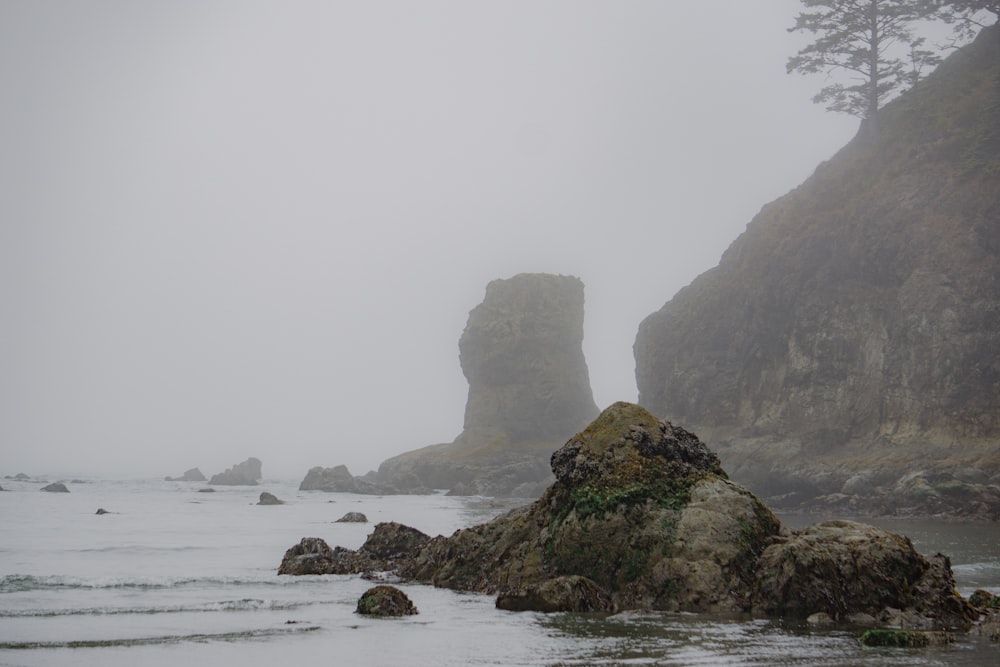 a foggy day at the beach with rocks in the foreground