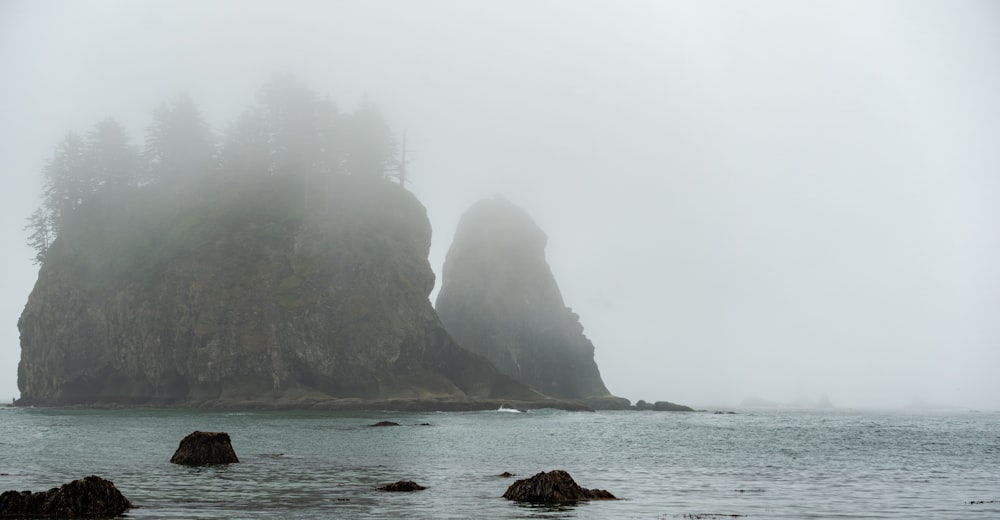 a foggy day at the ocean with a large rock formation