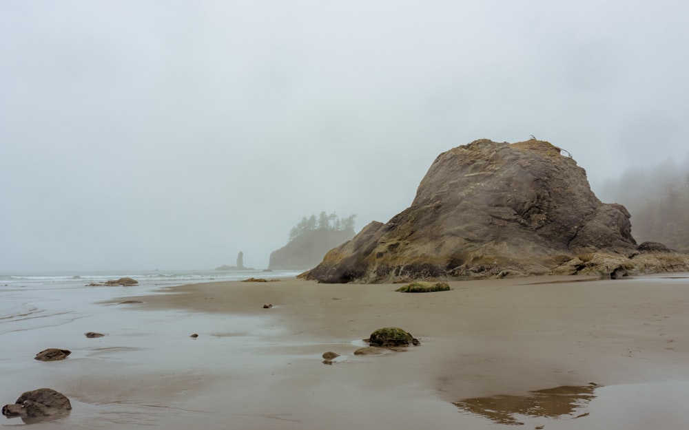 una gran roca sentada en la parte superior de una playa de arena