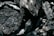 A close-up view of several pieces of charcoal, showcasing their rough textures and dark, ashy surfaces. The intricate details and patterns on each piece are highlighted by the lighting, which casts subtle shadows.