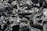 A close-up view of black charcoal pieces with a texture of ash and irregular surfaces. The dark chunks are interspersed with lighter gray ash, creating a rugged and textured composition.