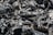 A close-up view of black charcoal pieces with a texture of ash and irregular surfaces. The dark chunks are interspersed with lighter gray ash, creating a rugged and textured composition.