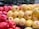 A vibrant display of red and yellow apples stacked together in a supermarket setting. The apples have shiny surfaces and visible stickers, indicating they are ready for sale. The background is blurred, focusing attention on the freshness and bright colors of the apples.