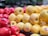 A vibrant display of red and yellow apples stacked together in a supermarket setting. The apples have shiny surfaces and visible stickers, indicating they are ready for sale. The background is blurred, focusing attention on the freshness and bright colors of the apples.