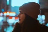 Profile of a person wearing a beanie against a backdrop of blurred neon lights, suggesting an urban night setting.