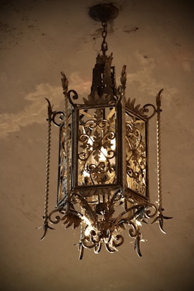 A vintage, ornate chandelier with intricate metalwork hangs from the ceiling. The chandelier features elaborate designs with leaves and scrolls, giving it a classic and elegant appearance.