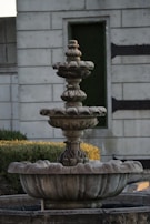 Rustic stone fountain with water gently flowing over carved details in a garden setting.