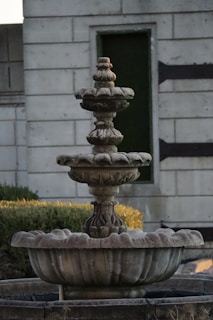 Rustic stone fountain with water gently flowing over carved details in a garden setting.