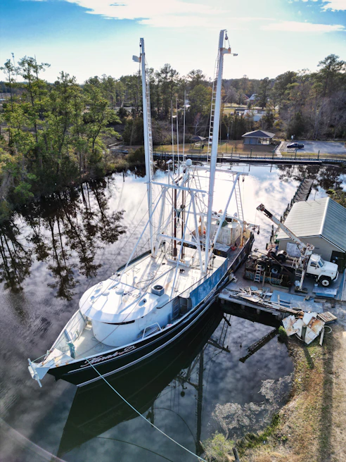 A sailboat docked with its mast being inspected and repaired by a technician