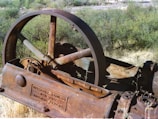 An old, rusted piece of industrial machinery with an engraved plaque showing Ingersoll-Rand Co., New York, Imperial Type 10. The machinery appears to be abandoned and situated in a natural environment with dry grass and various green shrubs.