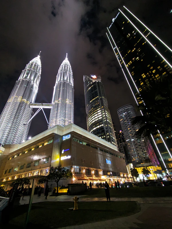 Petronas Twin Towers in Kuala Lumpur at night, dramatic dark sky, deep shadows, moody atmospheric city lights