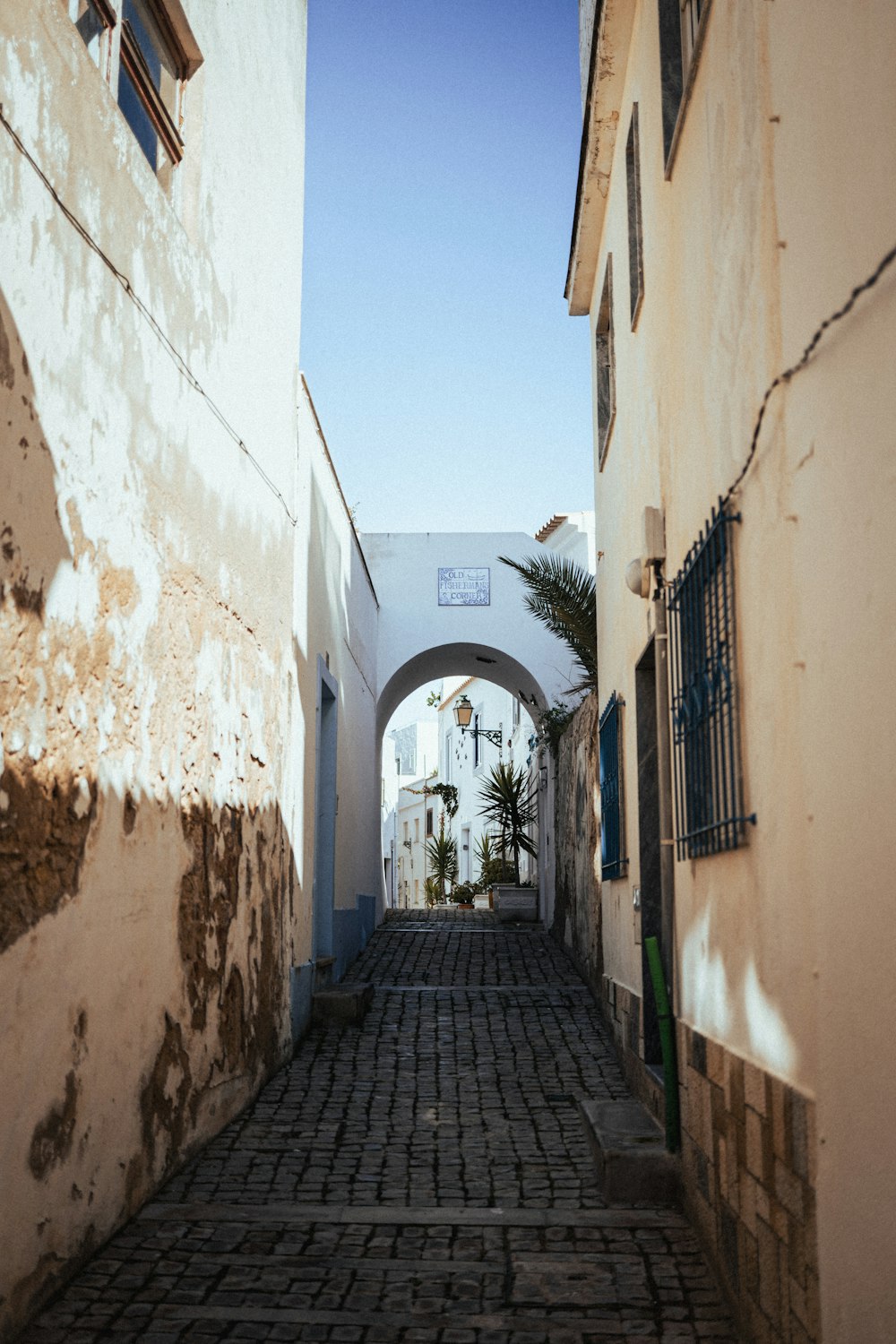 a narrow cobblestone street with an archway between two buildings