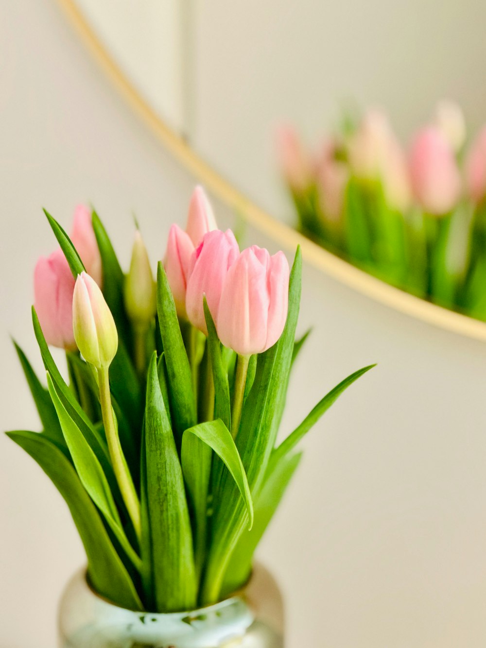 un vase rempli de tulipes roses à côté d’un miroir