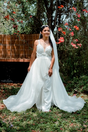 A bride in a flowing ivory lace gown standing in a sunlit garden.