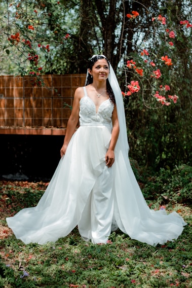 A bride glowing with natural makeup, standing on a sunlit terrace overlooking a serene beach at sunset.