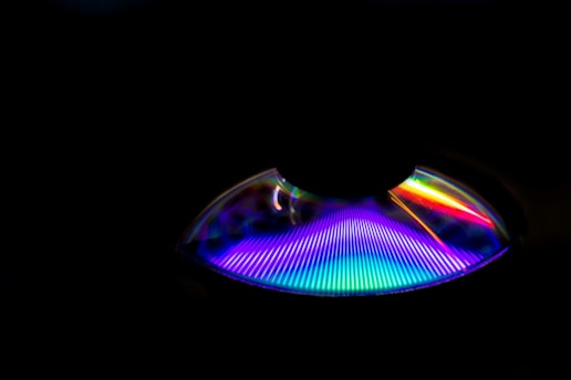 A dark background with a semi-circular, prism-like object emitting bright, multicolored light. The spectrum of colors includes blue, purple, red, pink, and green, creating a vivid and striking visual contrast.