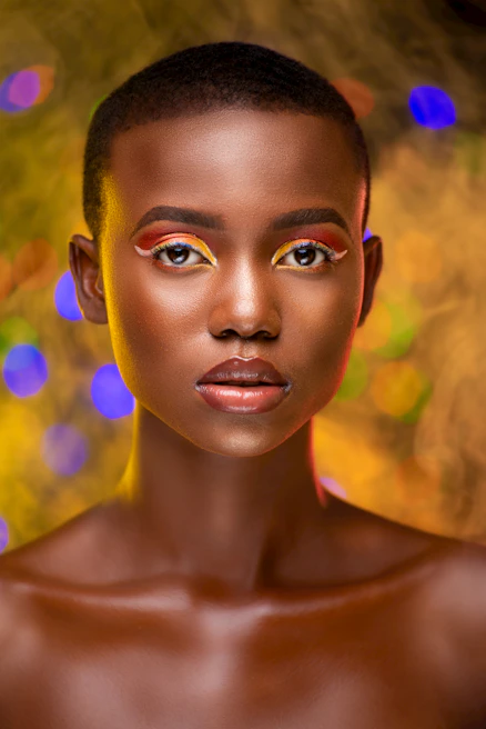 Fashion model showcasing bold, artistic makeup with shimmering eyeshadow and sleek hair against a minimalist backdrop