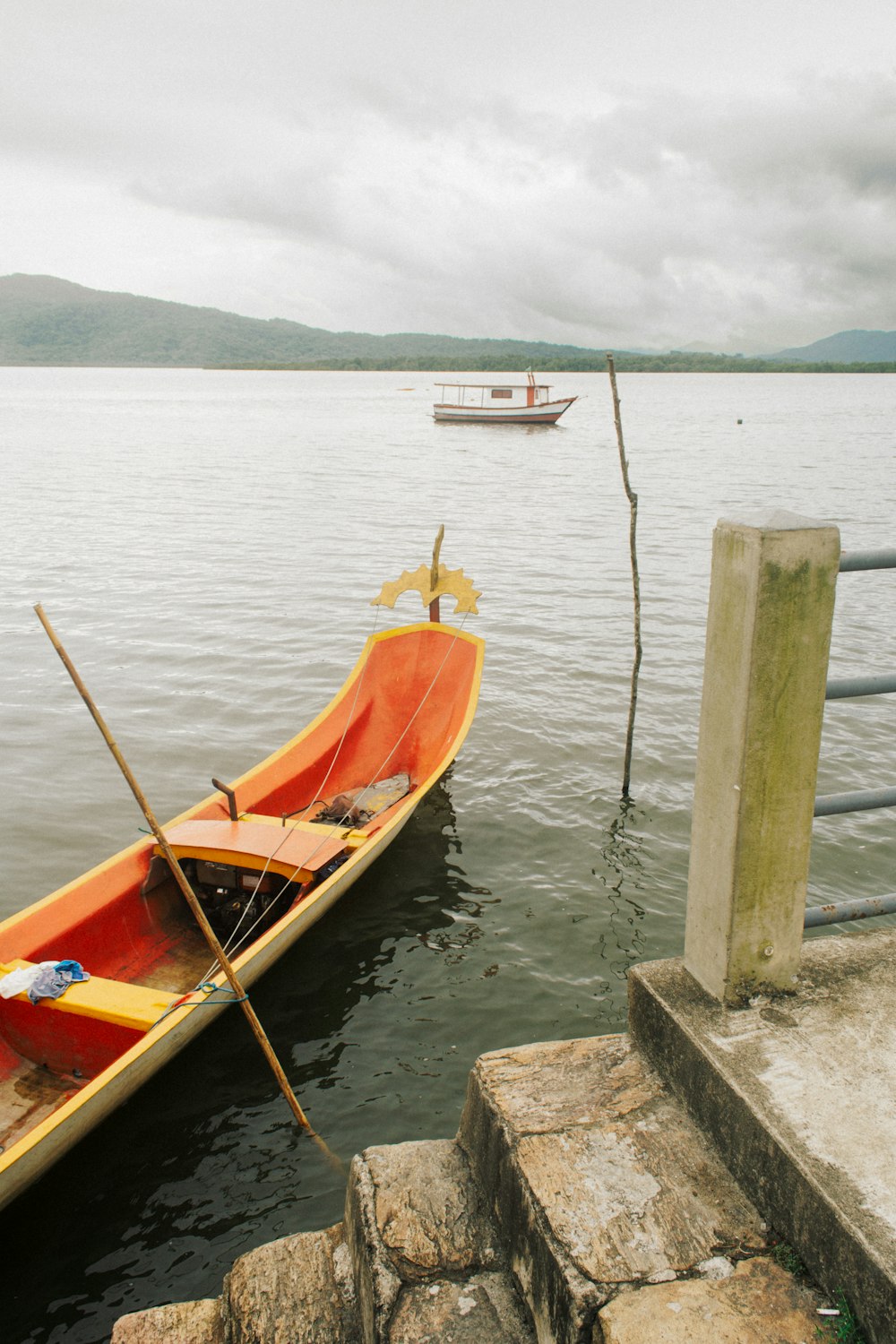 a red canoe tied to a dock with a boat in the background