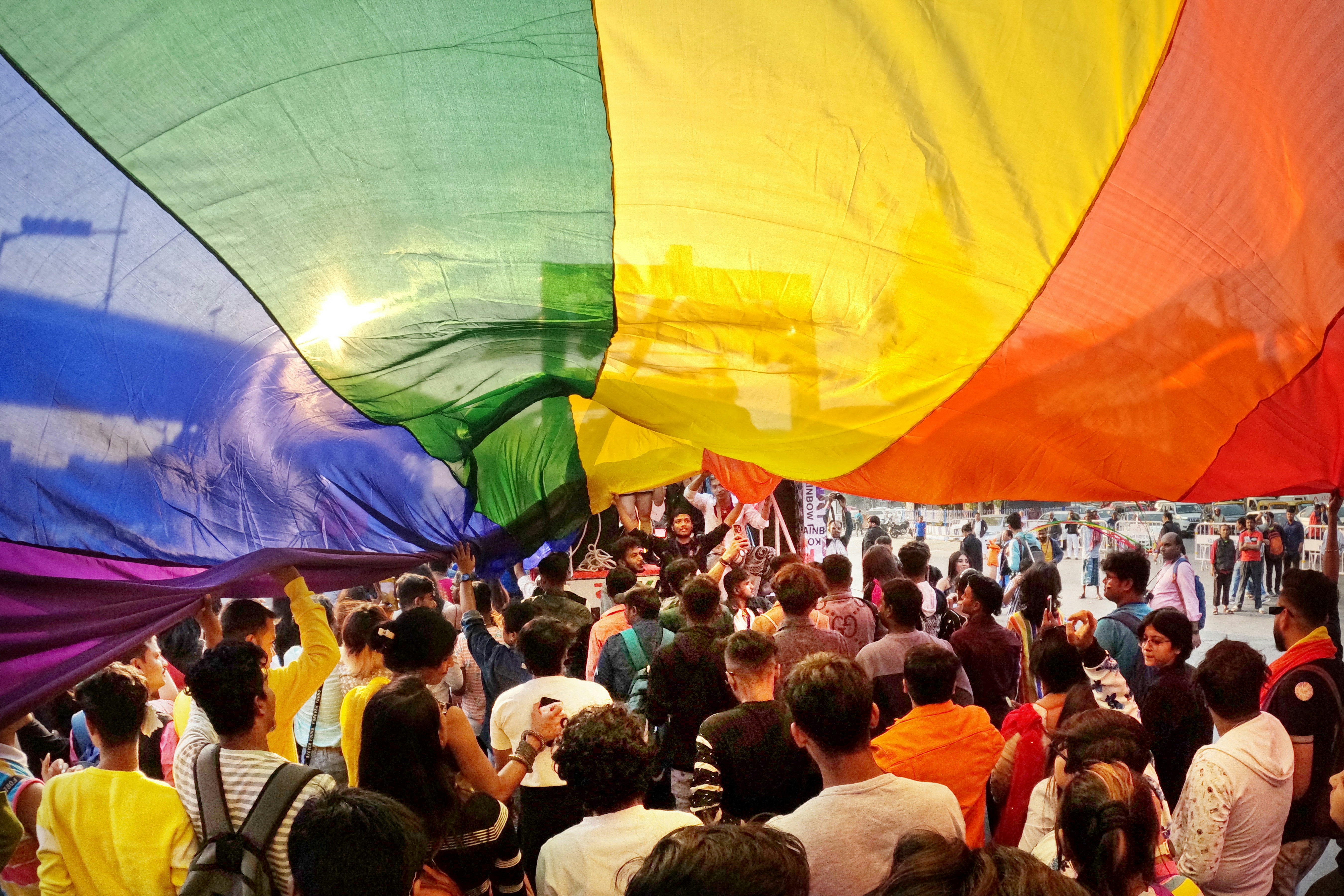 a crowd of people standing around a rainbow-colored kite
