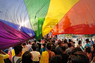 a crowd of people standing around a rainbow colored kite