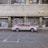 A red and white taxi is parked in front of a building with metal shutters that display graffiti art. The street is empty and the building appears to be old and slightly worn.