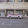 A red and white taxi is parked in front of a building with metal shutters that display graffiti art. The street is empty and the building appears to be old and slightly worn.