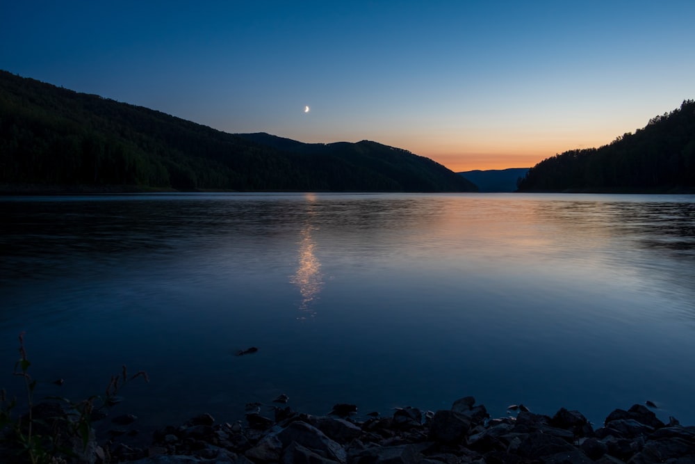 the sun is setting over a lake with mountains in the background