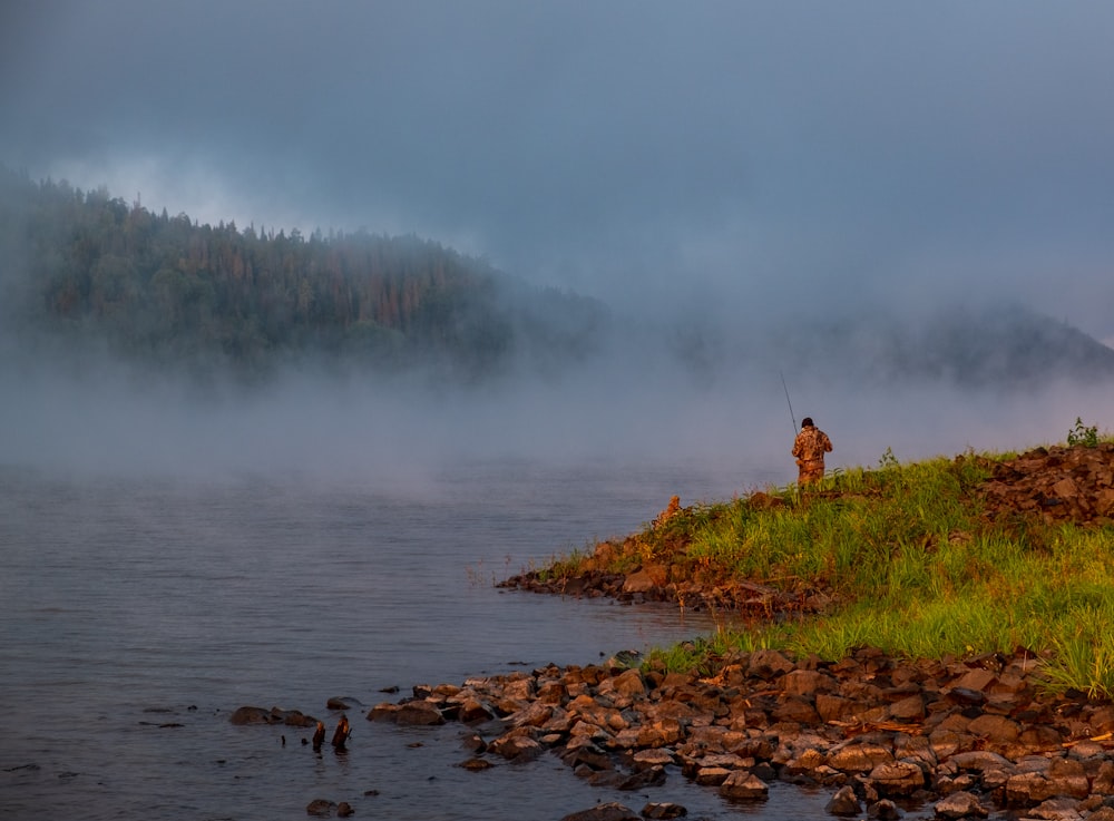 a man standing on a hill next to a body of water