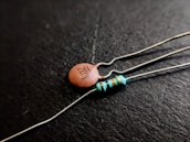 Close-up shot of two electronic components on a black background; one is a ceramic capacitor with '103Z' printed on it, and the other is a resistor with colored bands.