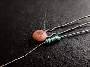 Close-up shot of two electronic components on a black background; one is a ceramic capacitor with '103Z' printed on it, and the other is a resistor with colored bands.
