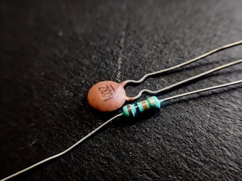 Close-up shot of two electronic components on a black background; one is a ceramic capacitor with '103Z' printed on it, and the other is a resistor with colored bands.
