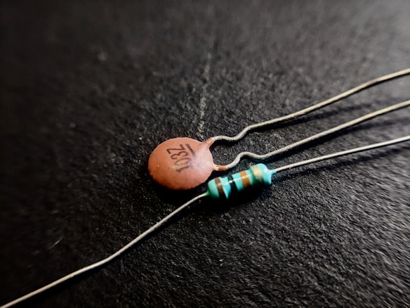 Close-up shot of two electronic components on a black background; one is a ceramic capacitor with '103Z' printed on it, and the other is a resistor with colored bands.