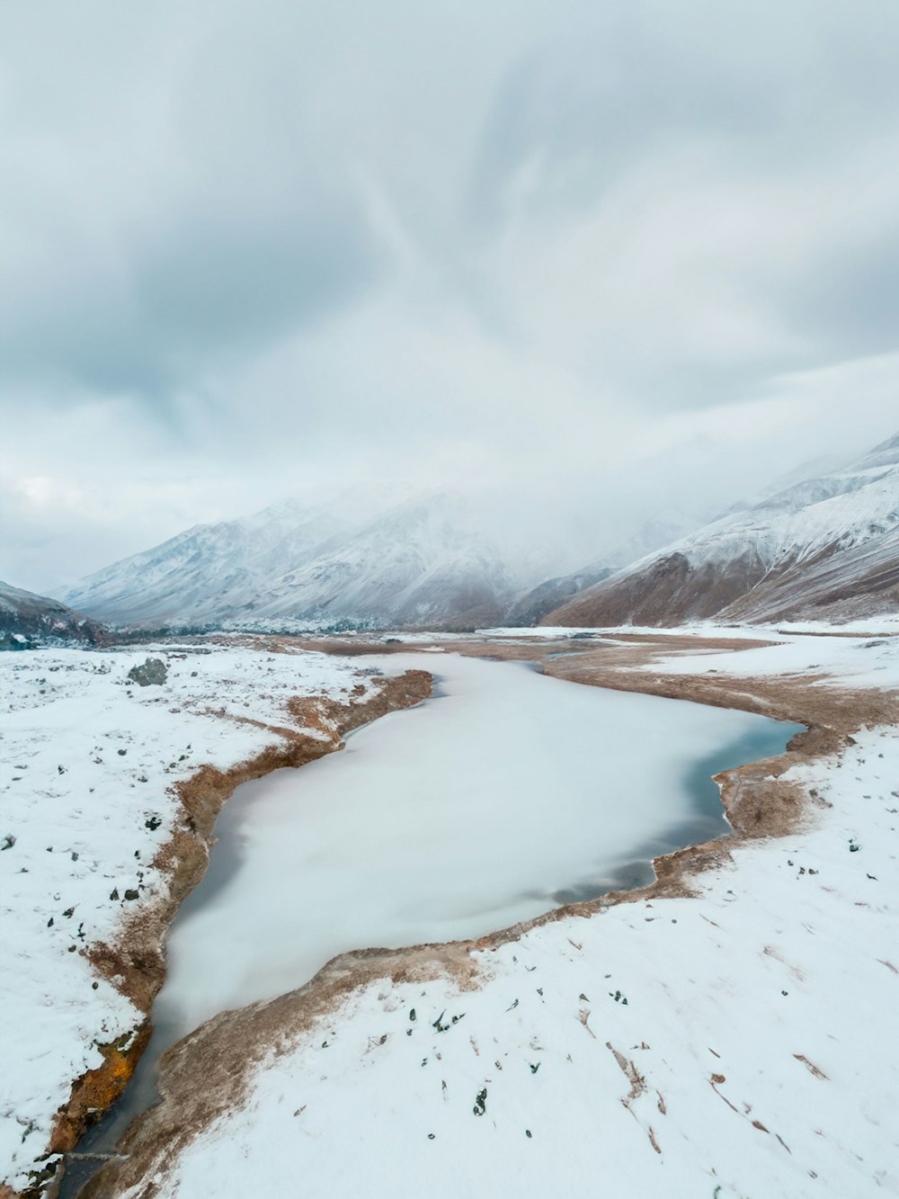 a frozen lake surrounded by snow covered mountains